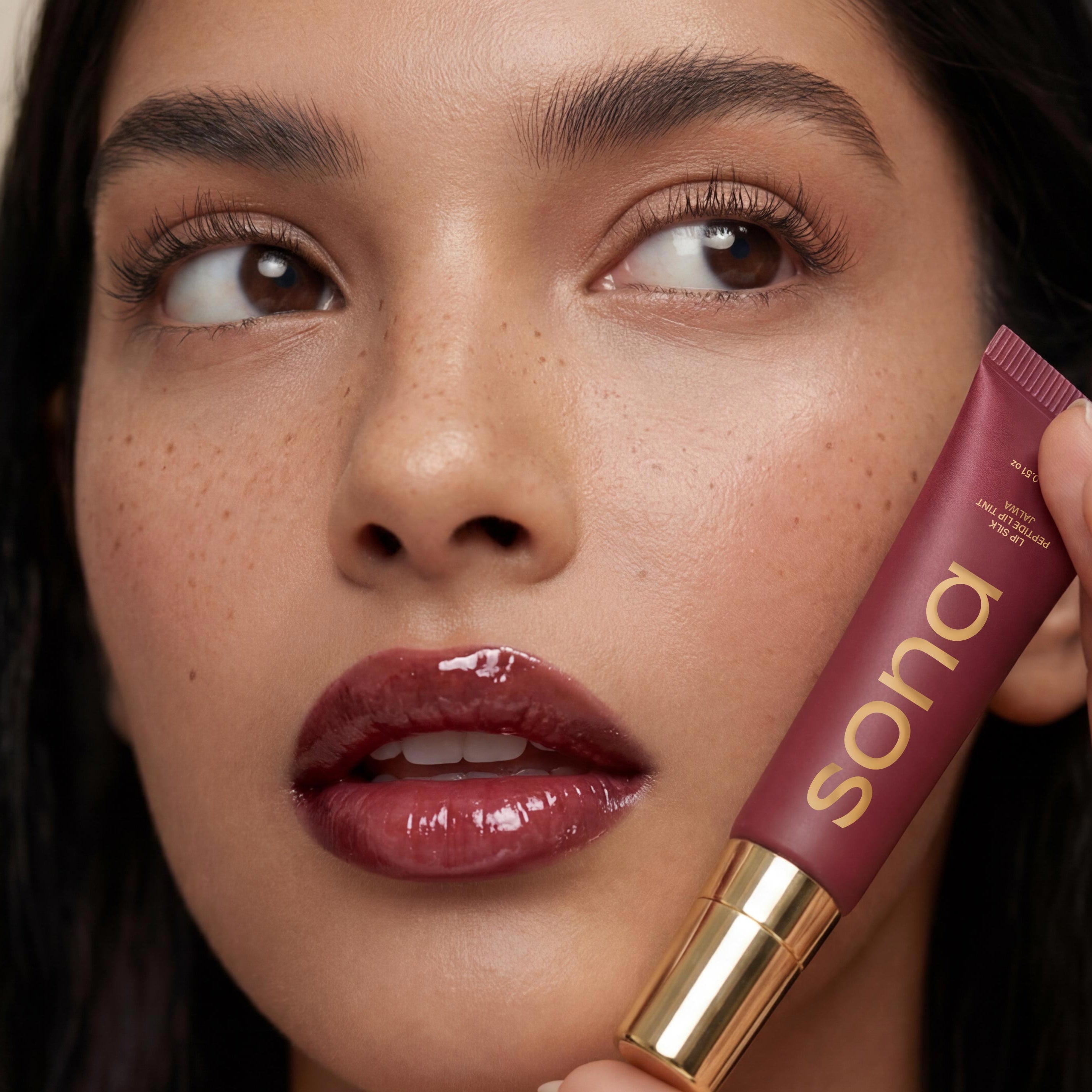 Woman holding a purple lipstick with 'Sona' branding against a beige background